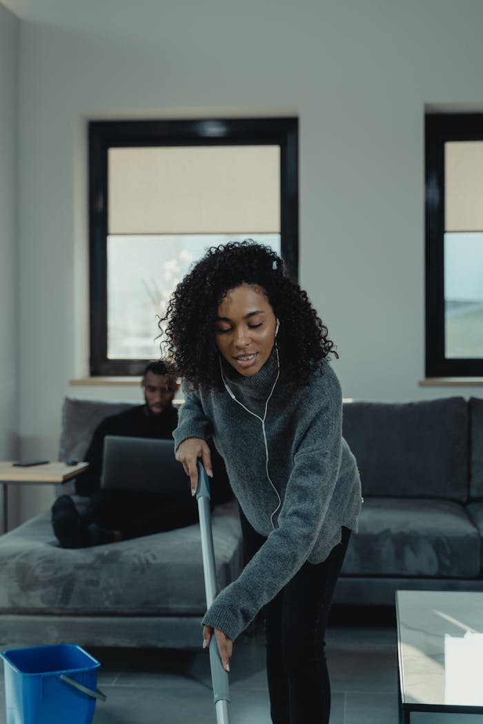 Mastering the First Impression: Your intriguing post title goes here Young woman mopping the floor while listening to music in a cozy living room setting on a sunny day.