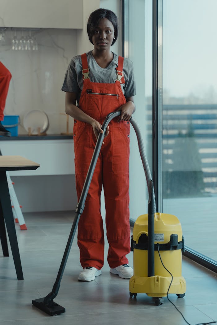 The Art of Drawing Readers In: Your attractive post title goes here An adult woman in red coveralls operates a vacuum cleaner in a modern indoor setting, focusing on cleaning tasks.